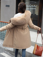 Person wearing a beige parka with a fur-lined hood, walking on a street.