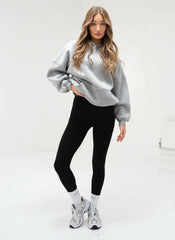 Woman wearing a gray sweater, black leggings, and white sneakers on a white background