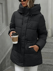 Person wearing a black puffer coat holding a coffee cup against a neutral background