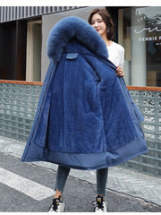 Woman wearing a blue coat with a large fur hood on a city street.