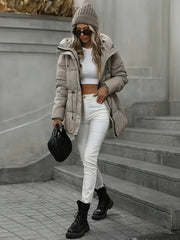 Person wearing a beige puffer jacket, white crop top, and white pants standing on steps.