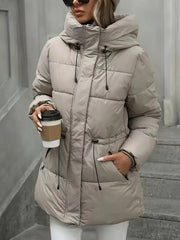 Person wearing a beige puffer coat holding a coffee cup against a neutral background