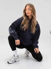 Woman wearing a navy oversized sweatshirt and black pants on a white background