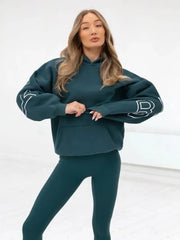 Woman wearing a green sweatshirt and leggings with white lettering on a white background