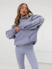 Person wearing a light purple hoodie and leggings with a brand logo on a white background